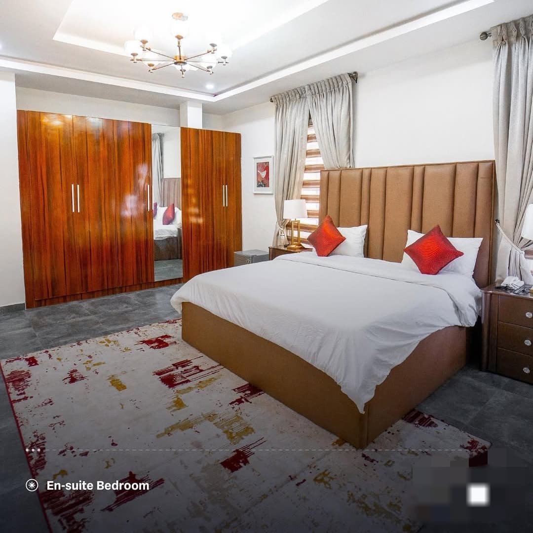 En-suite bedroom with brown upholstered bed, red accent pillows and wooden wardrobe