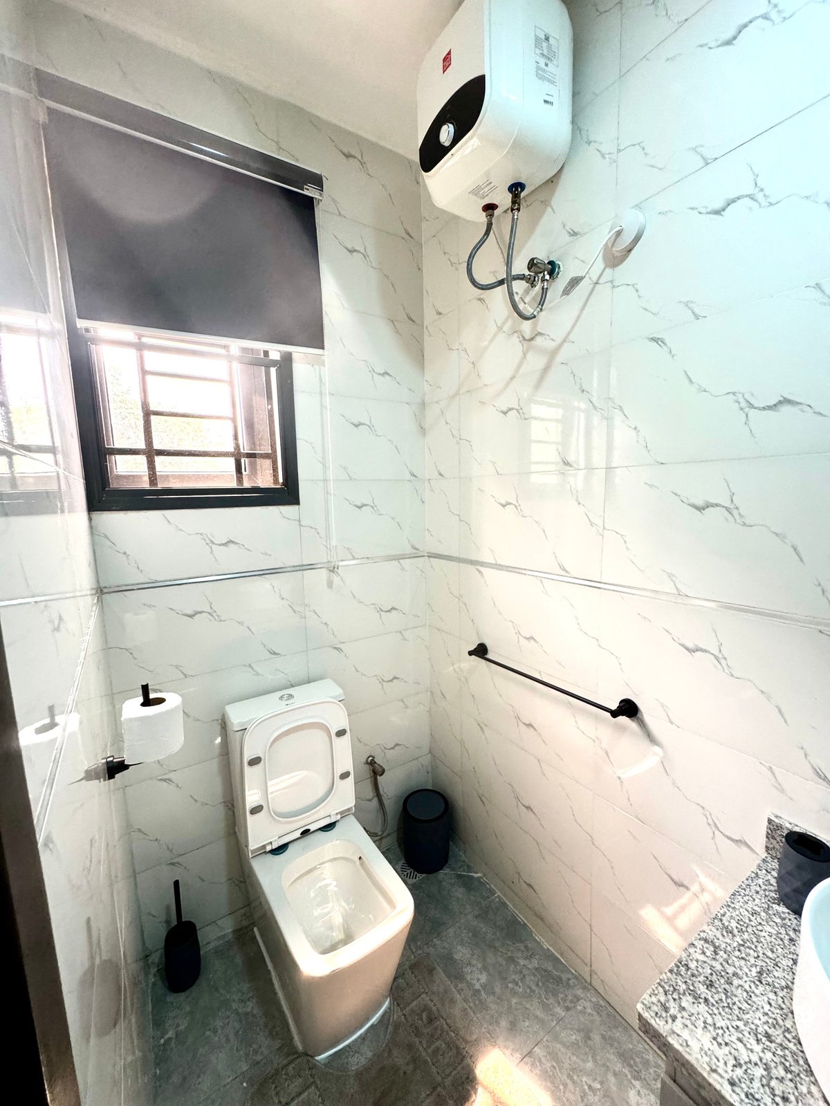 Bathroom with marble-look tiled walls, white toilet, instant water heater and dark tile flooring
