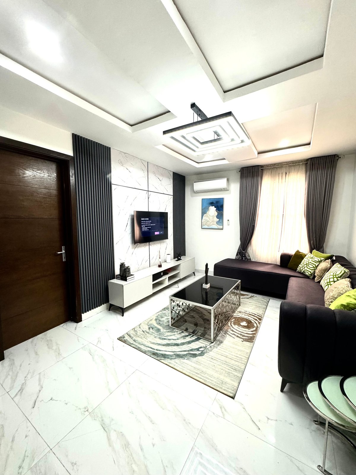 Living room with marble flooring, dark sofa, wall-mounted TV and minimalist furniture
