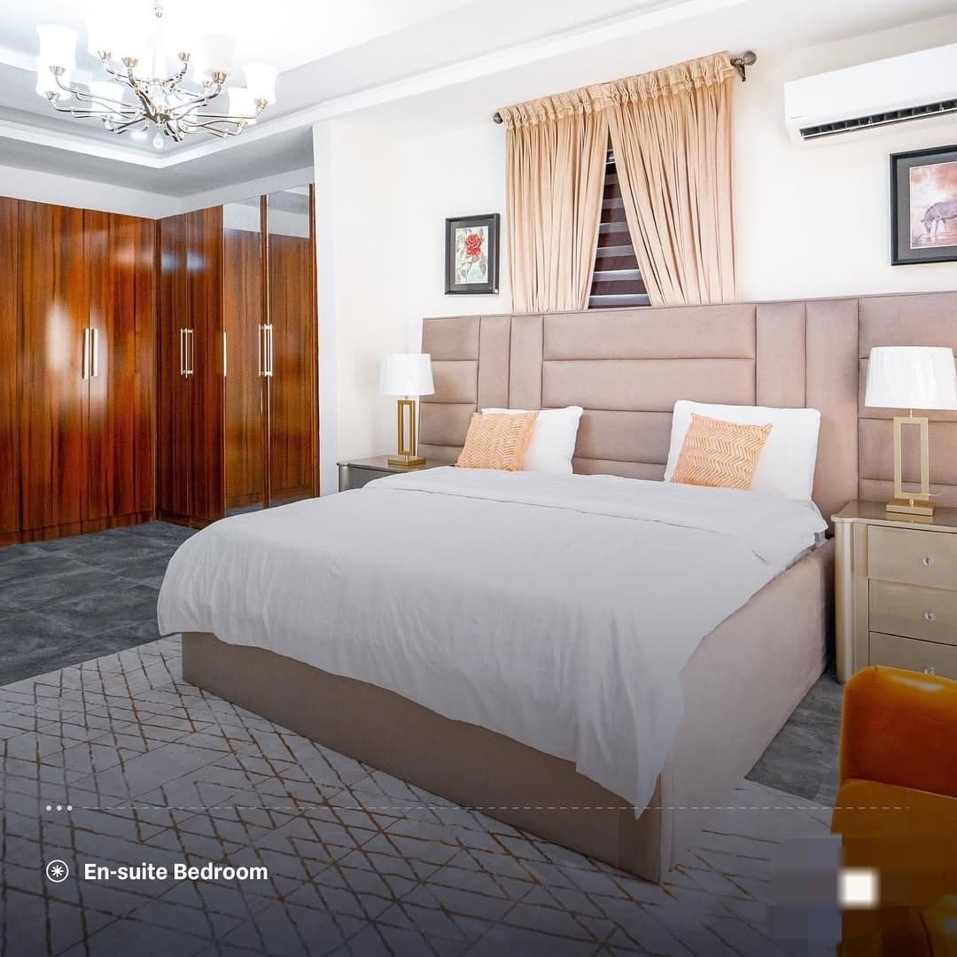 En-suite bedroom with beige upholstered bed, cream curtains and wooden wardrobe