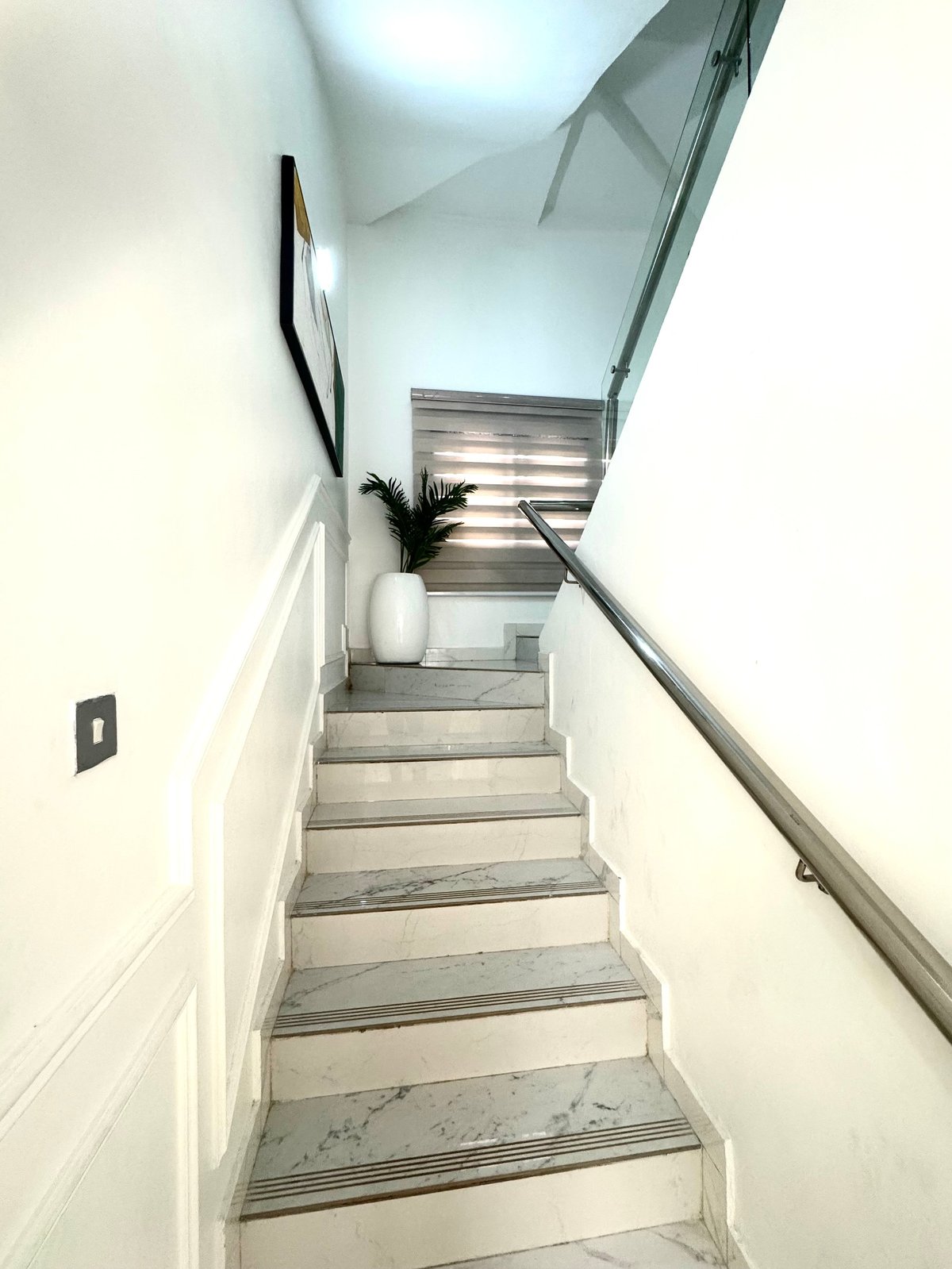 Modern staircase with gray steps, metal handrail, white walls and skylight window