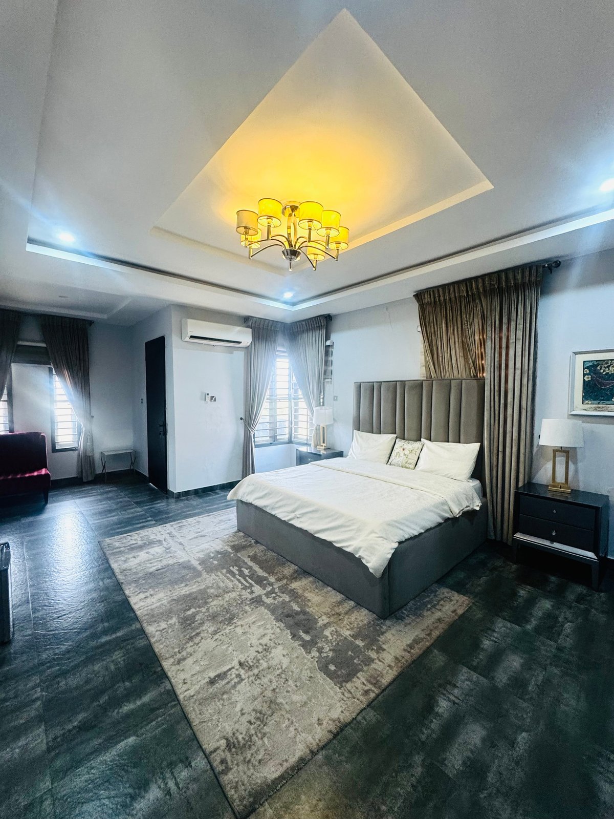 Master bedroom with large bed, gray upholstered headboard and gold chandelier