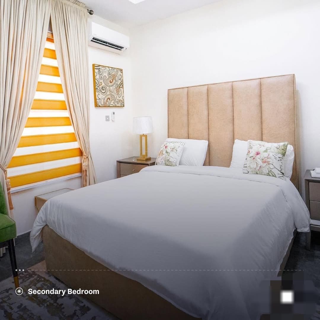 Secondary bedroom with upholstered headboard, white bedding and yellow-striped curtains