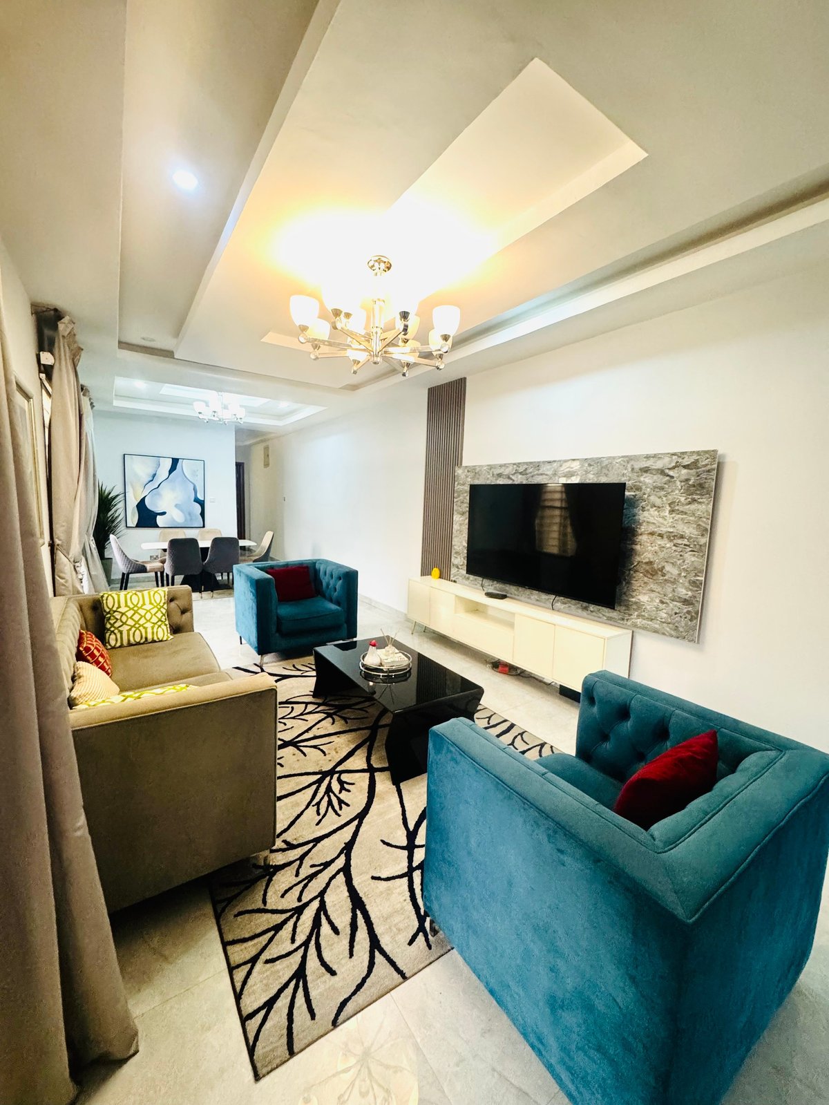 Living room with teal velvet seating, wall-mounted TV and geometric ceiling