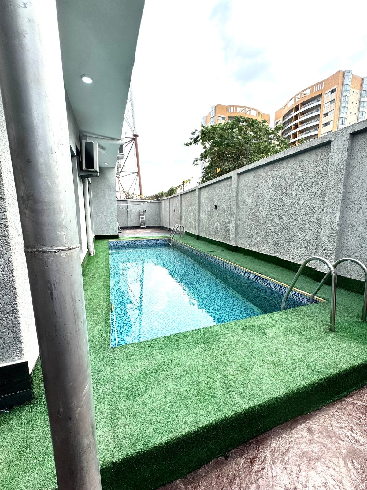 Rooftop swimming pool with artificial green turf surrounded by concrete walls